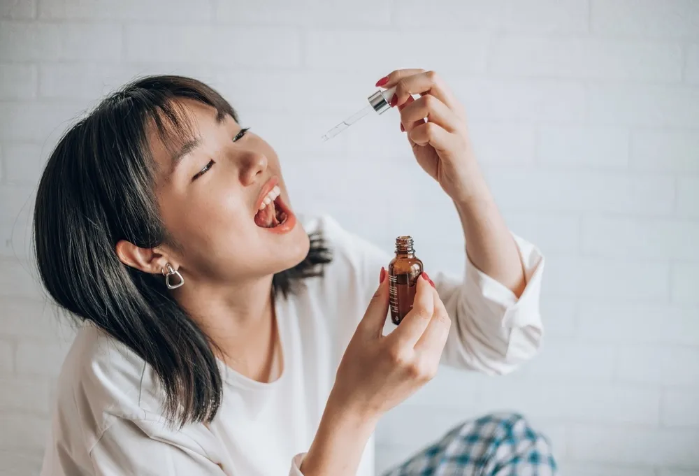 A woman takes her oral medication from a dropper.
